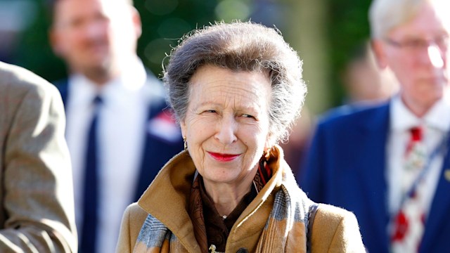 Princess Anne reading a book and smiling while wearing red lipstick