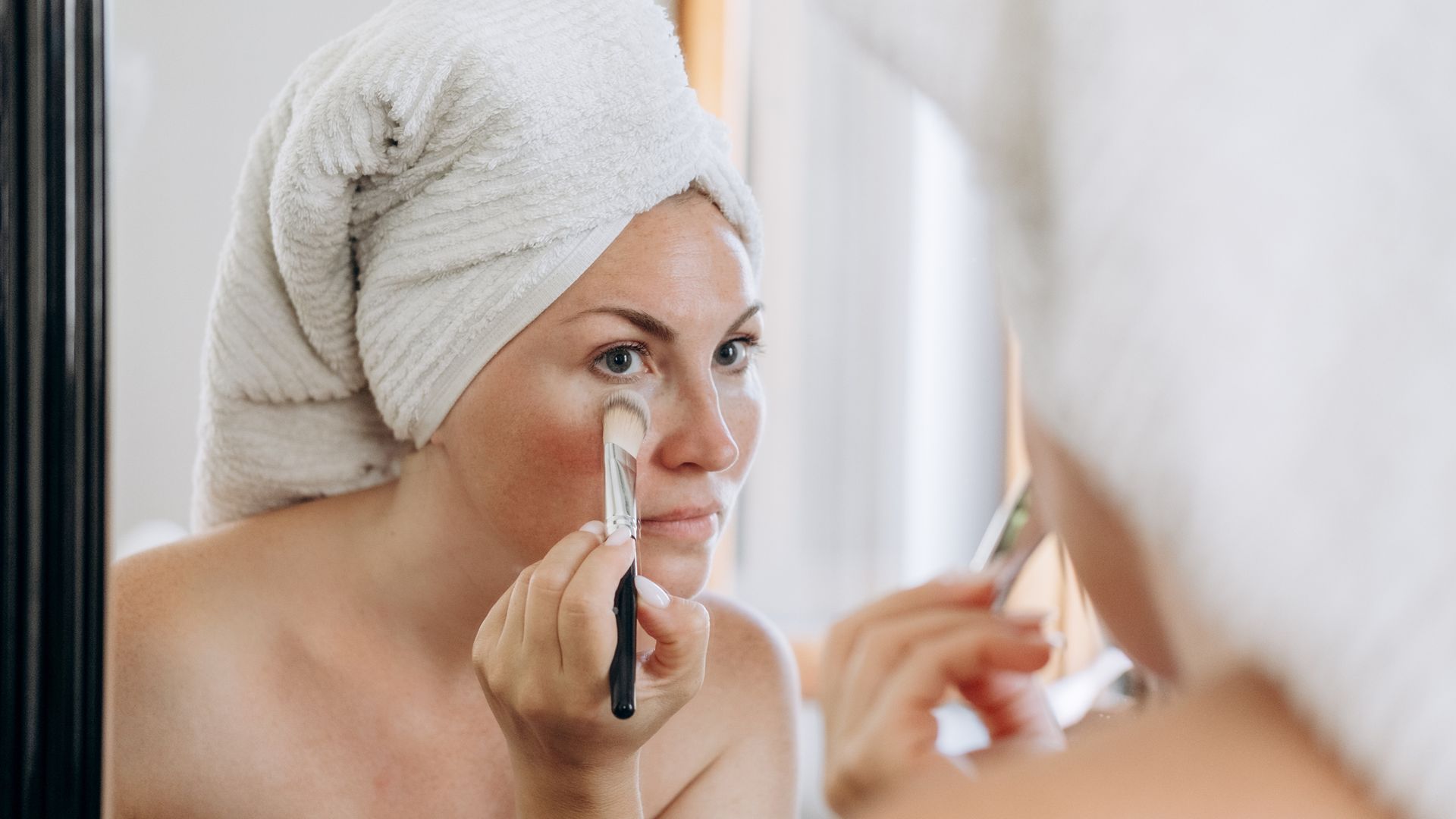 woman applying concealer in bathroom mirror.