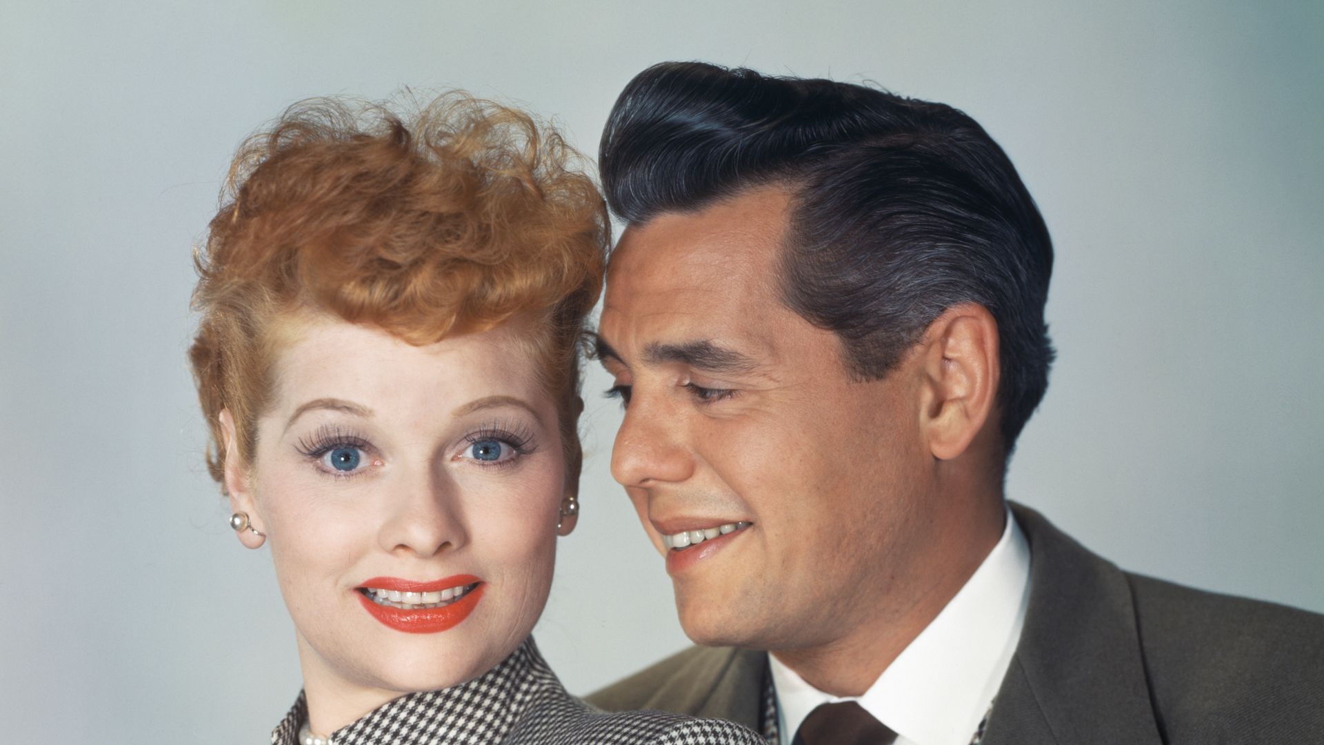 American actress and comedian Lucille Ball, wearing a black-and-white checked high collar outfit with a pearl choker, beside her husband, Cuban-born American actor, musician and comedian Desi Arnaz, in a publicity portrait for their sitcom 'I Love Lucy', United States, circa 1953