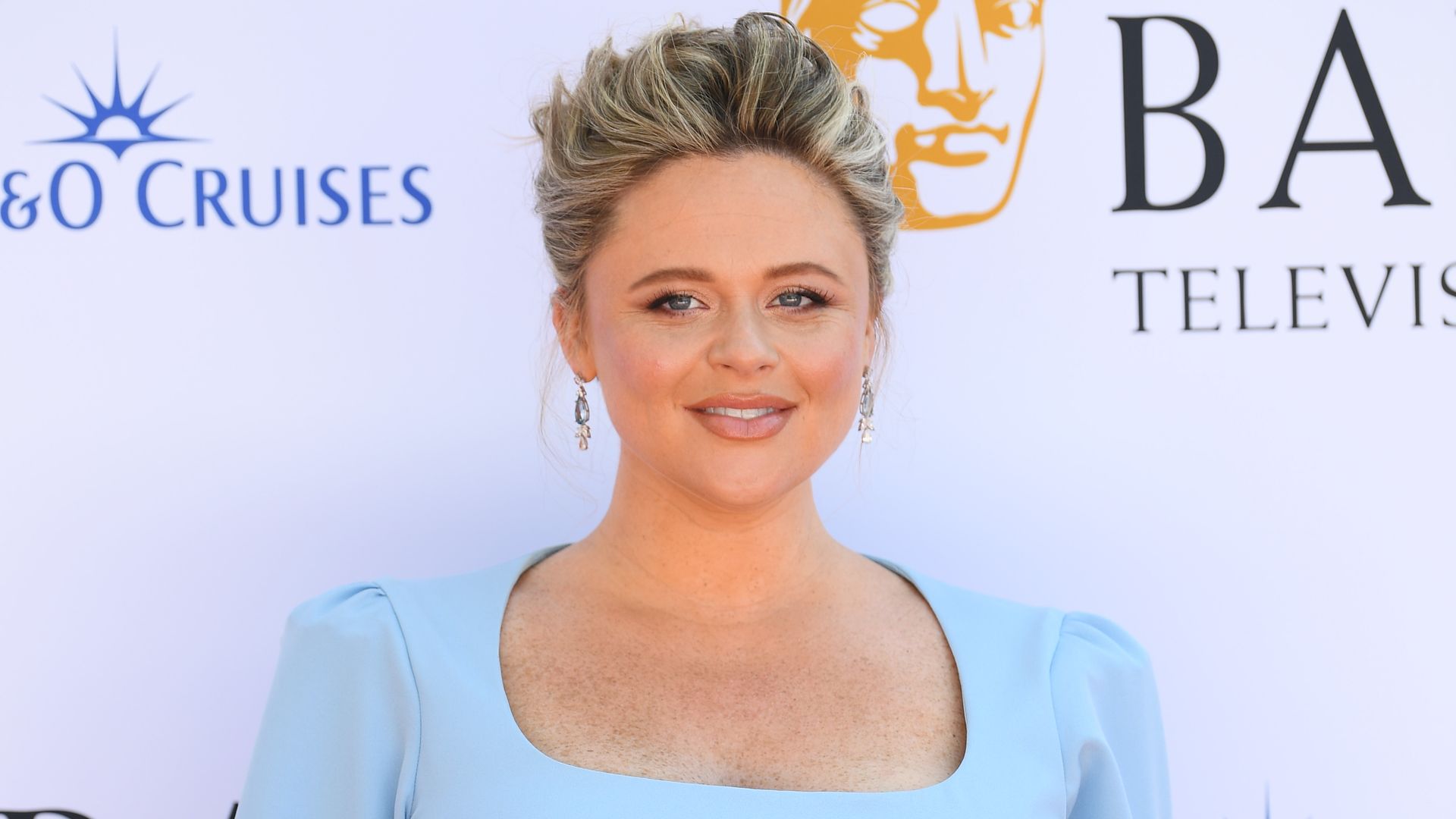 Emily Atack cradling her baby bump in a baby blue dress