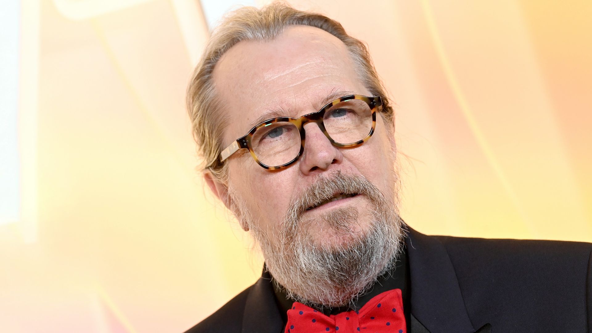 Gary Oldman in a black suit and a red bowtie