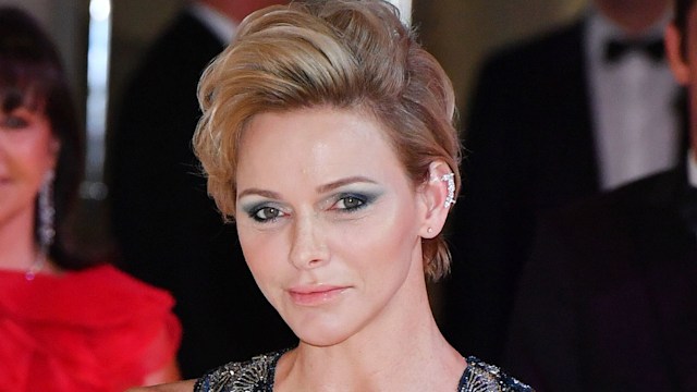 Princess Charlene of Monaco with black mermaid dress heavy eye makeup and blonde quiff