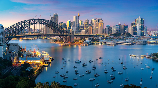 Cityscape image of Sydney, Australia with Harbor Bridge and Sydney skyline during sunset.