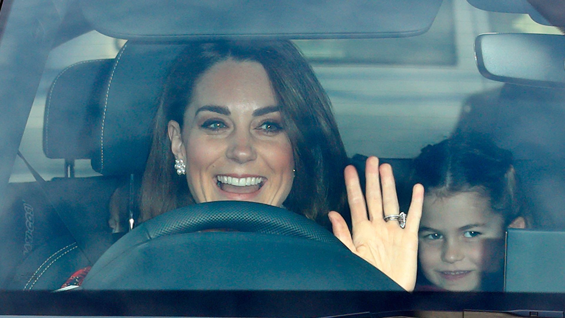 Kate Middleton waving while driving with Princess Charlotte in the back
