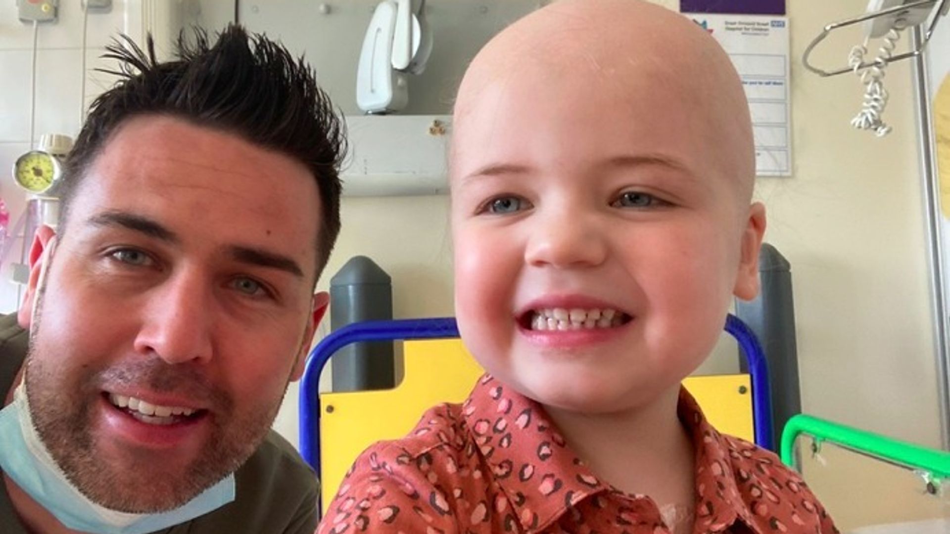 man with little girl with no hair smiling in hospital bed 