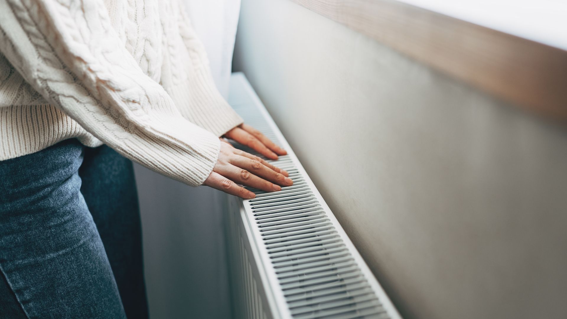 Central heating problem at home. Woman checking heating radiator in cold apartment