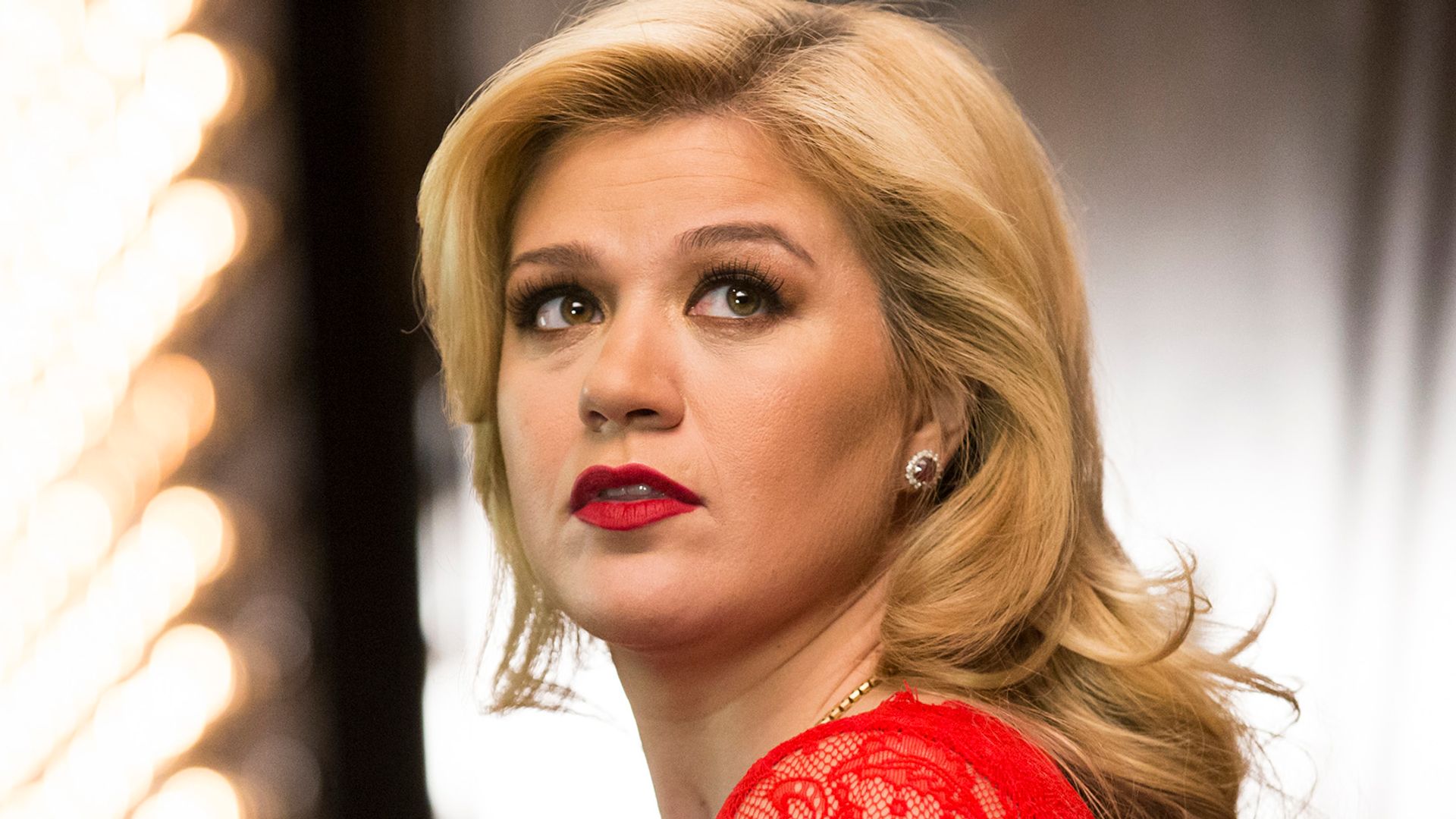 Kelly Clarkson in a red lace dress and red lipstick looking into the distance