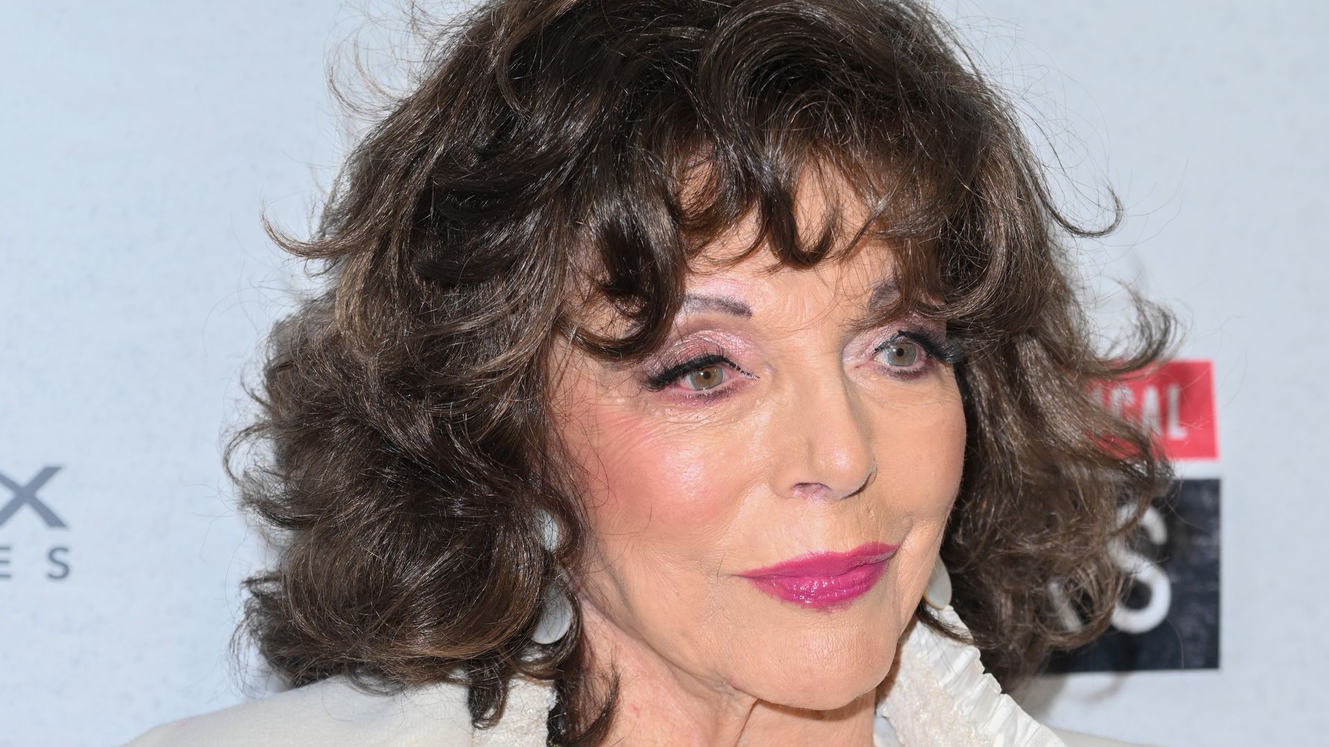 Dame Joan Collins looking to right in white coat