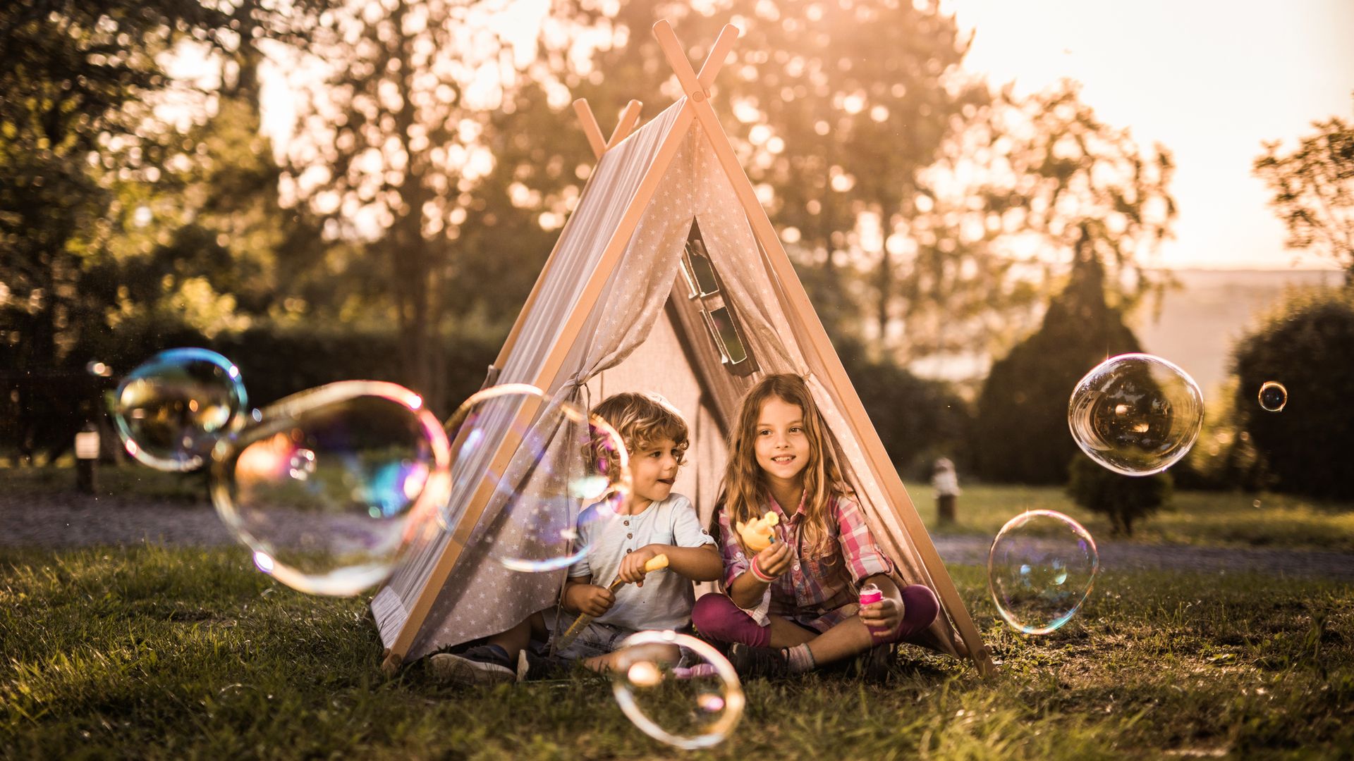Two small siblings sitting in a tent in the backyard and playing with bubble wand