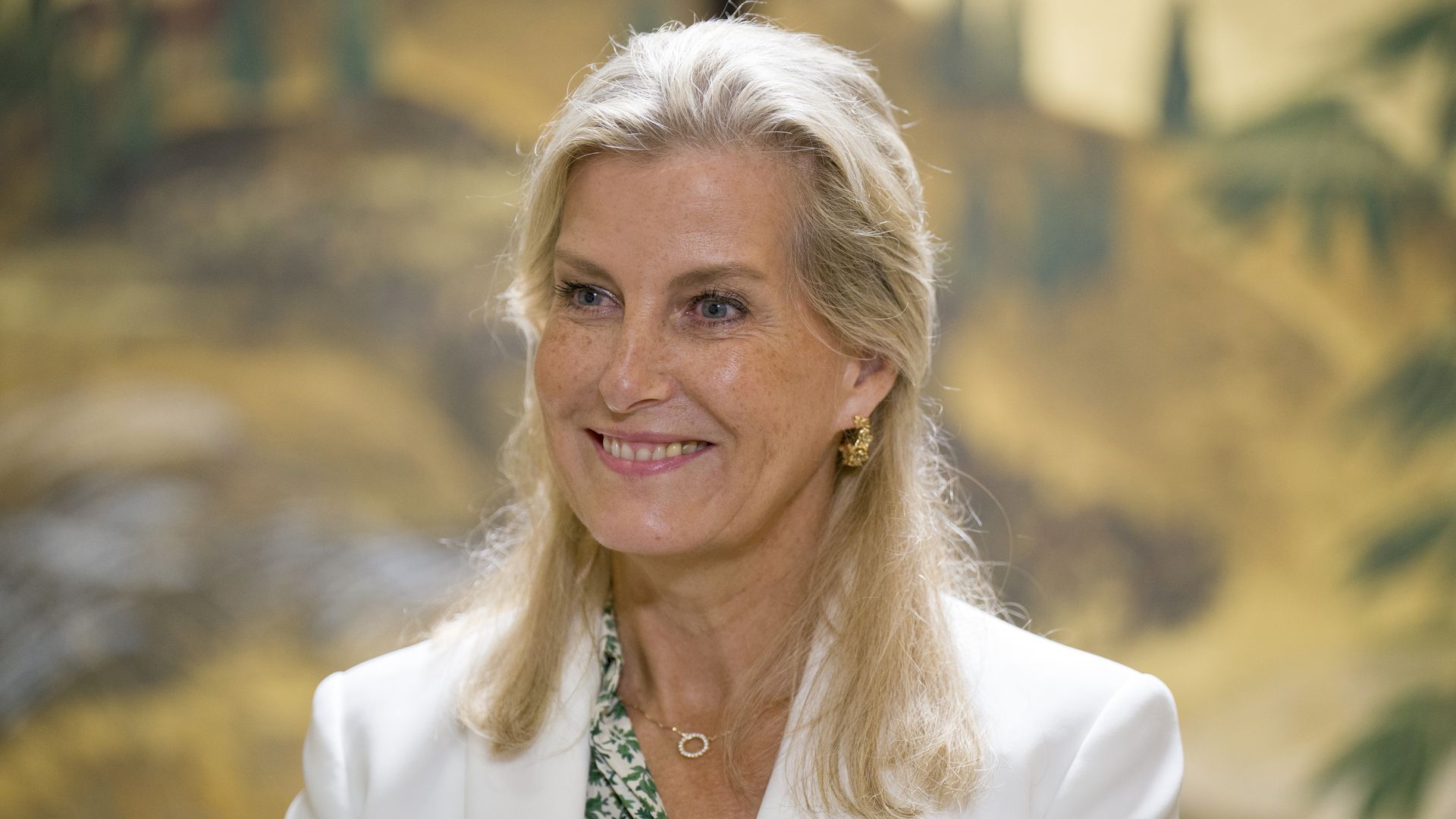 The Duchess of Edinburgh smiling to left in white blazer and green floral dress