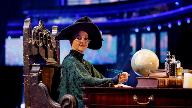 Sarah Hadland as Professor Minerva McGonagall sitting at a desk