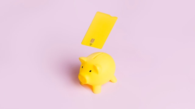 Elevated view of yellow piggy bank and credit card on yellow background