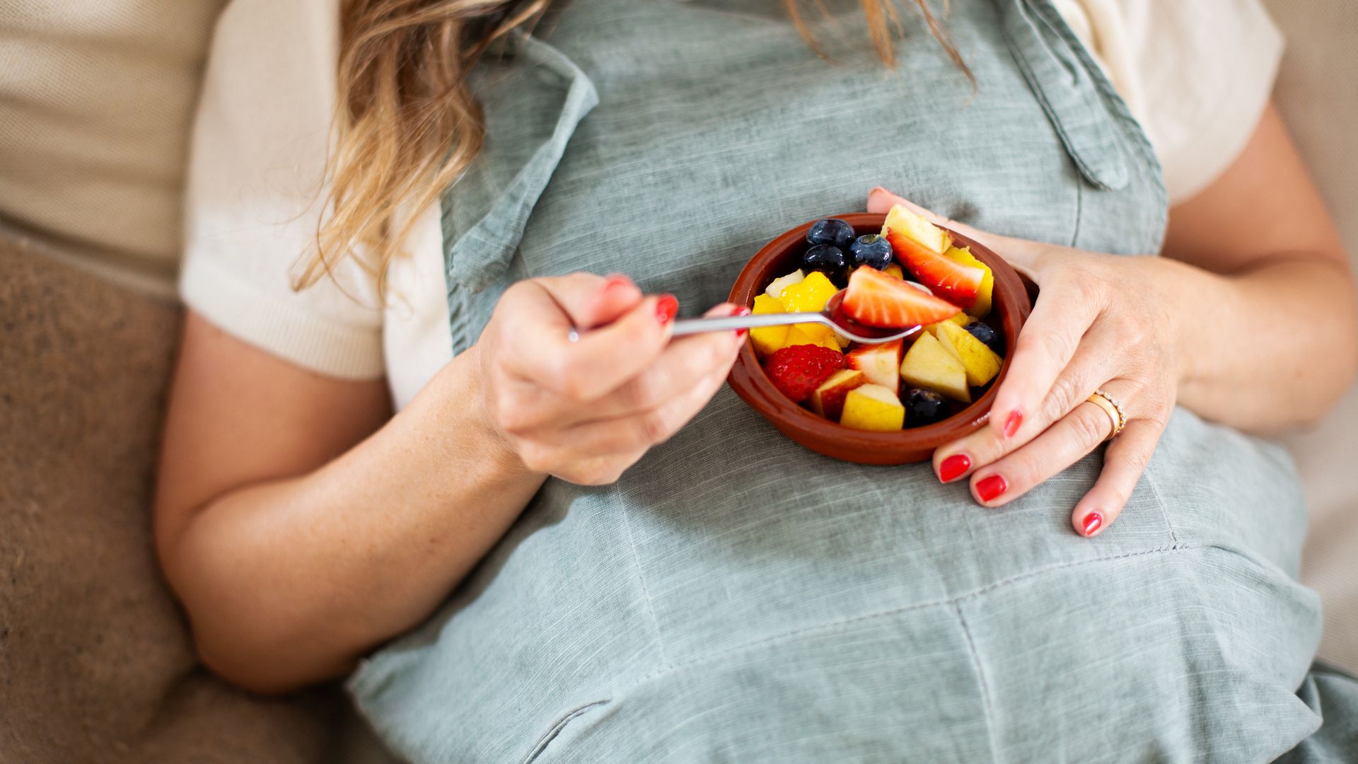 Pregnant woman eating fruit salad, midsection