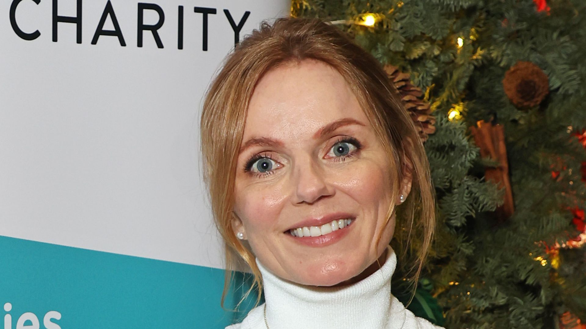 Geri Halliwell-Horner in white dress stood in front of a sign for the Rainbow Trust