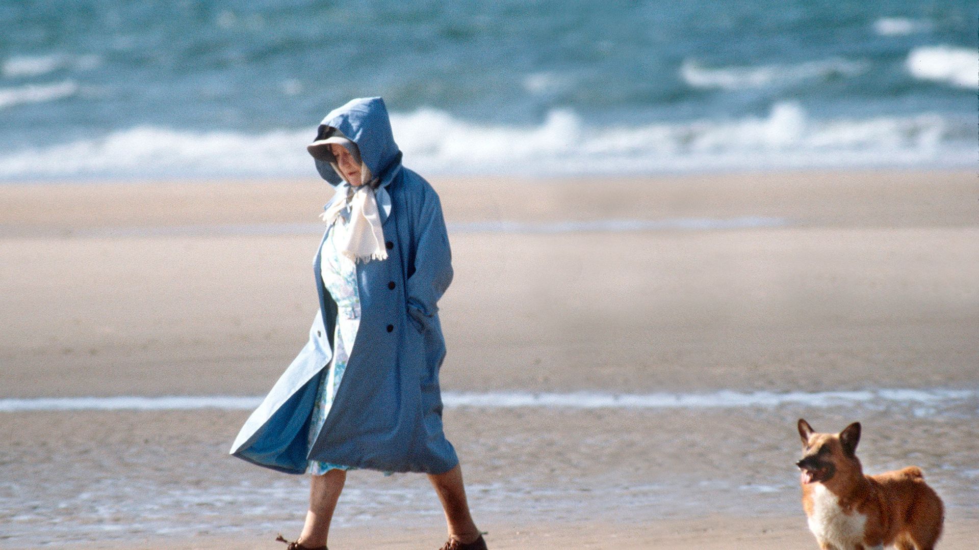 queen mother walking along beach with corgi