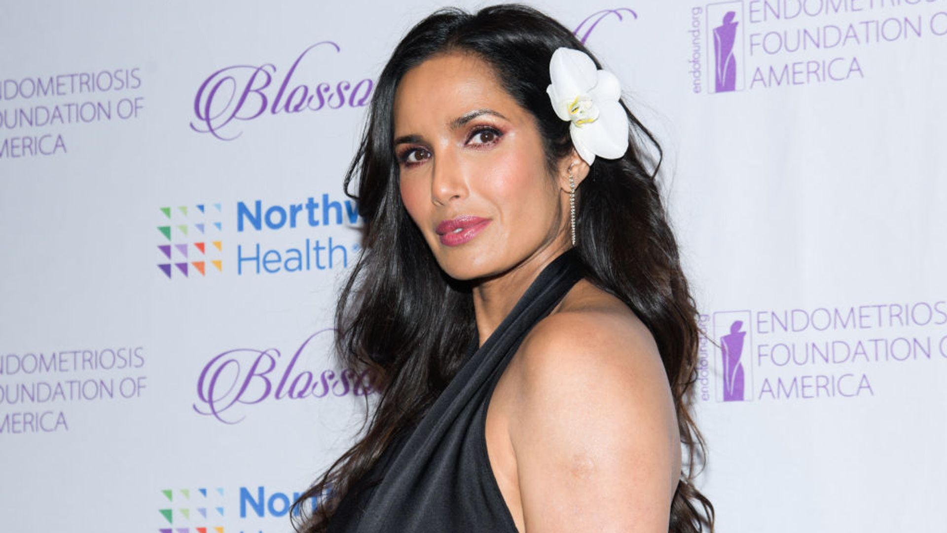Padma Lakshmi at the Blossom Ball Endometriosis Foundation of America held at Cipriani 42nd Street on March 20, 2023. She is wearing a black satin halterneck dress and has a white orchid in her hair. 