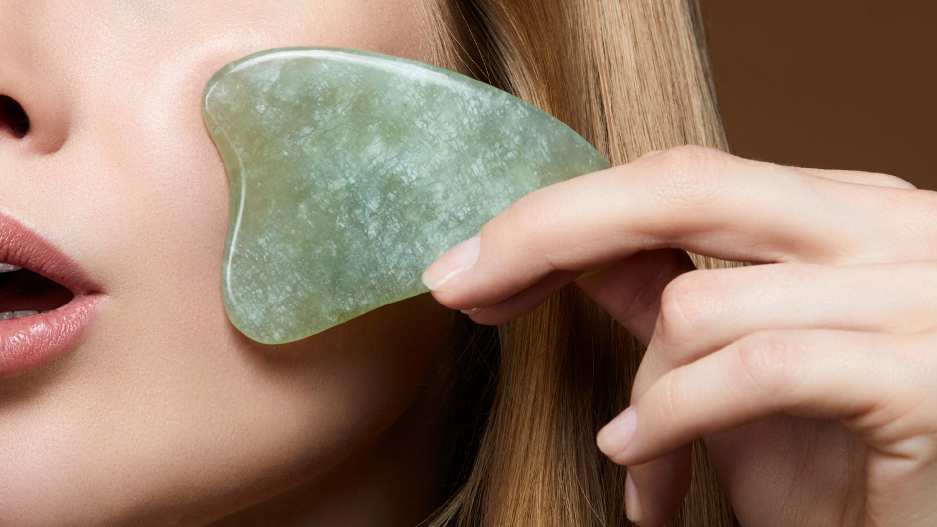 woman massaging her face to avoid wrinkles with a scraping jade Gua Sha Massage tool- asian skin care beauty trend