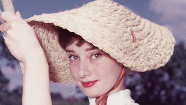 Portrait of Belgian-born American actress Audrey Hepburn (1929 - 1993) as she wears a peculiar hat and sleeveless blouse and holds a pool cleaning net beside a dry swimming pool, early 1950s