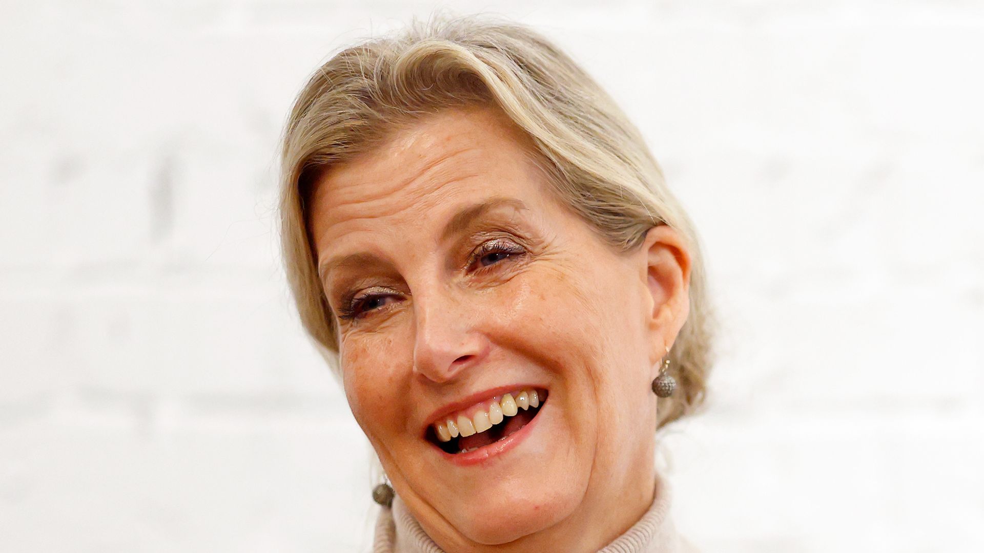 Sophie, Duchess of Edinburgh sitting laughing in oatmeal rollneck dress
