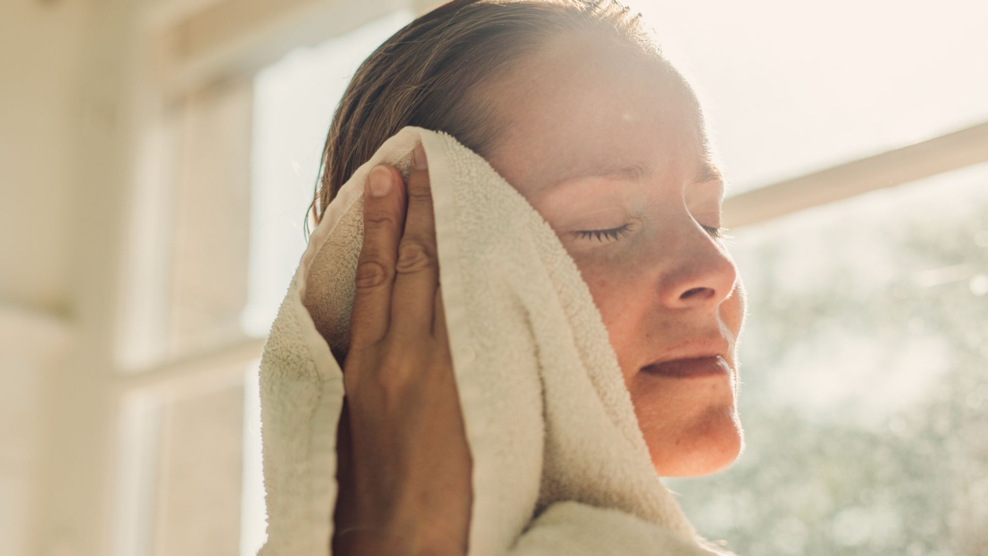 Woman toweling face after bathing in sunny bathroom.
