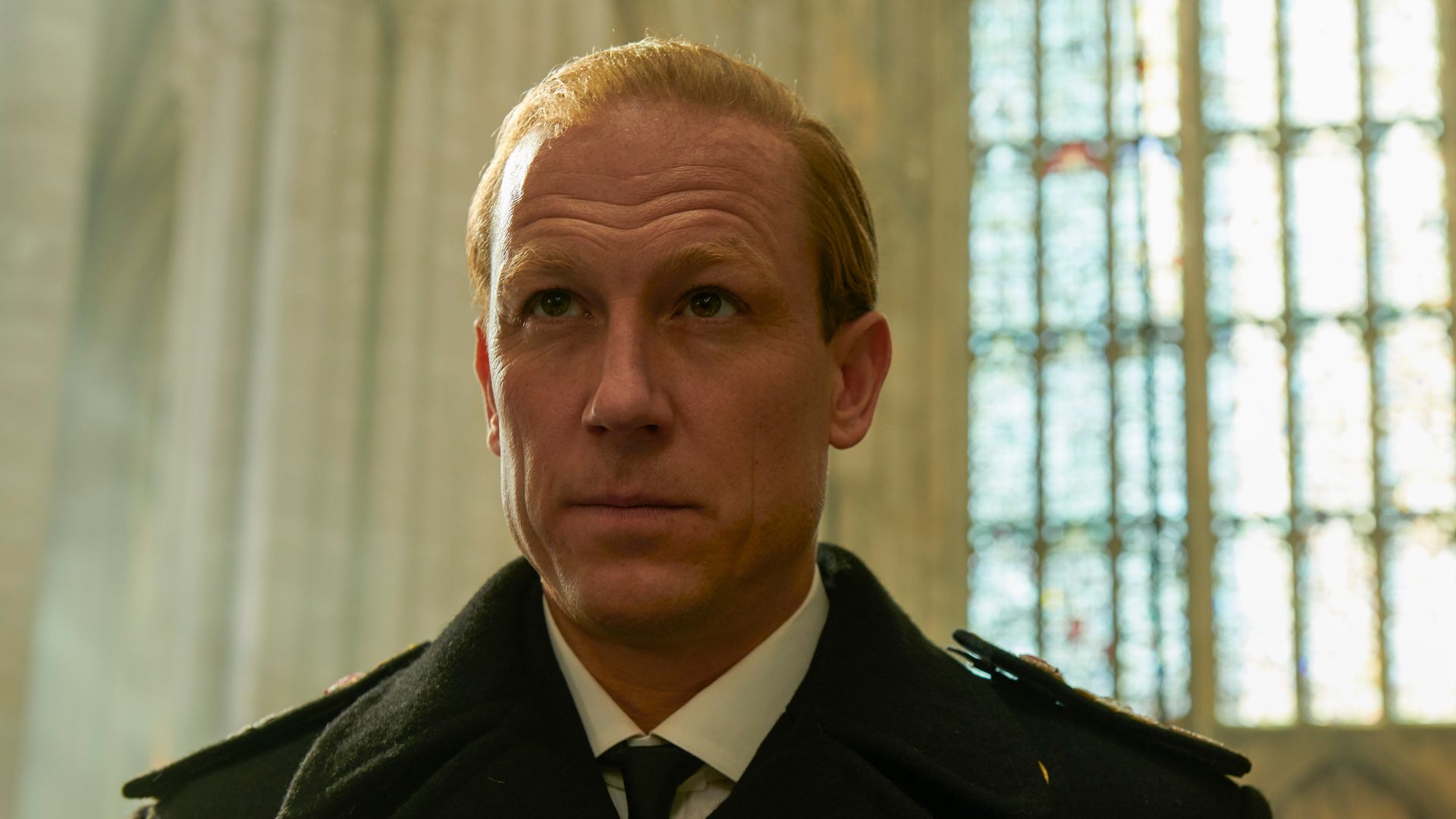 A man stands in a church with a formal coat on