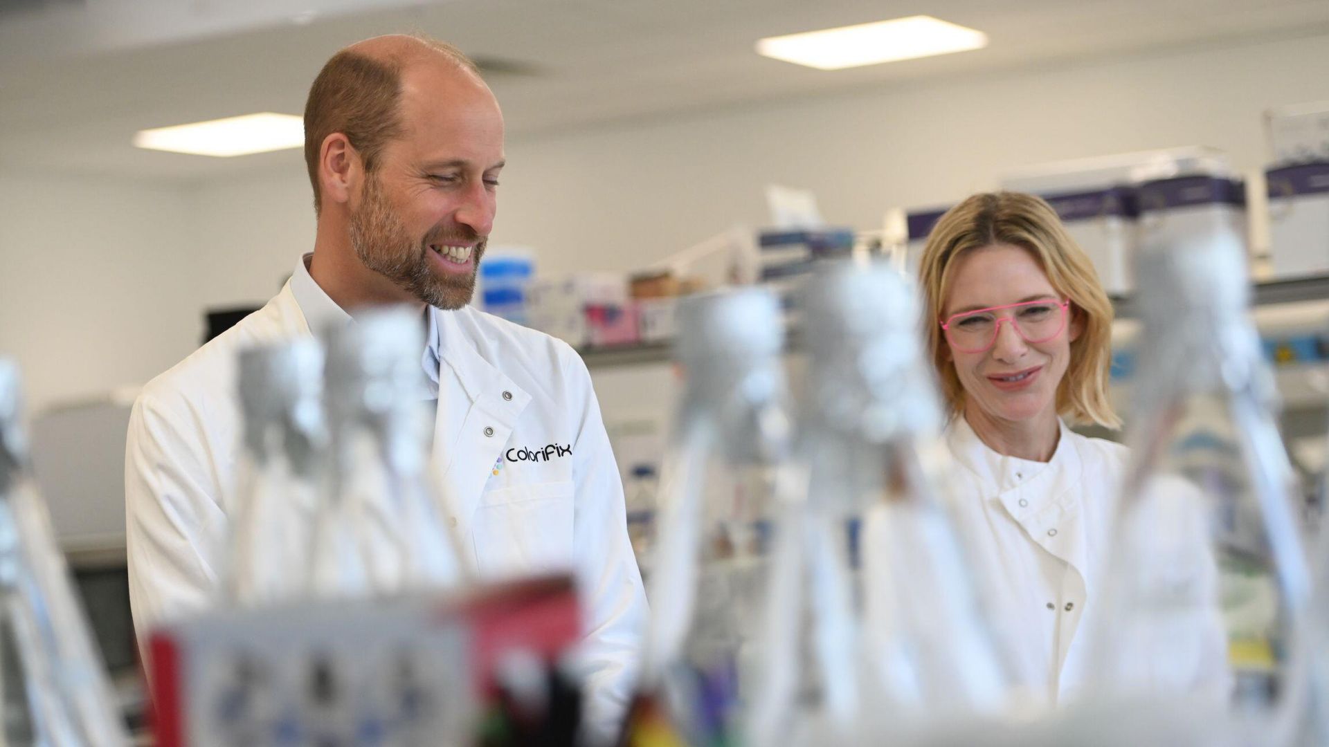 Prince William and Cate Blanchett in lab coats looking at scientific equipment
