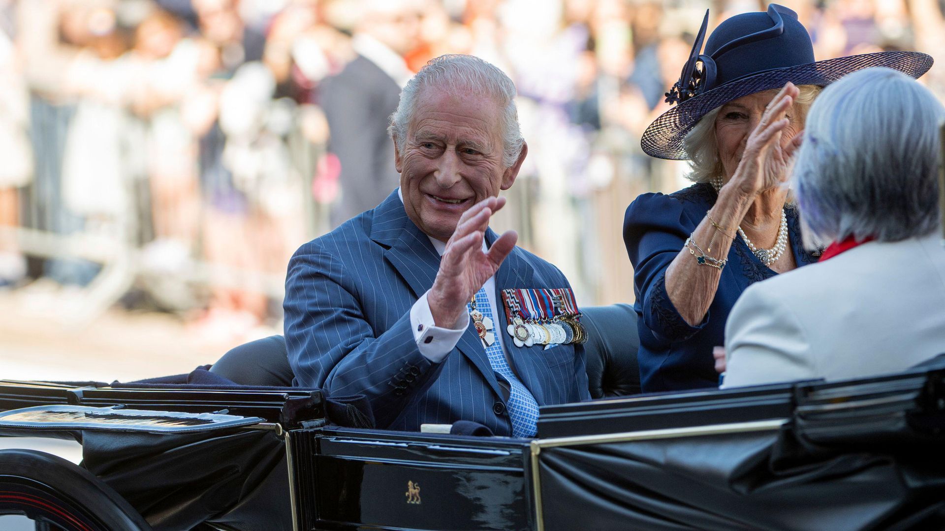 King Charles and Queen Camilla waving from a carriage