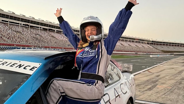 Sydney Sweeney sitting on the side of a race car with her arms in the air