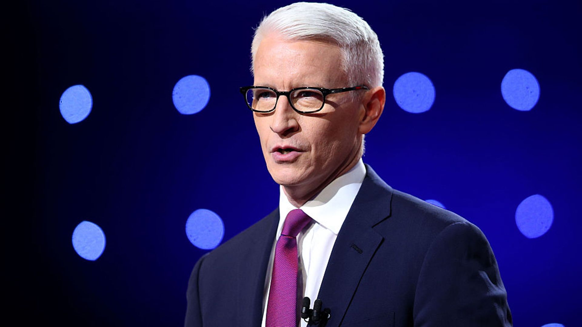 Close up on Anderson Cooper wearing a navy suit. 