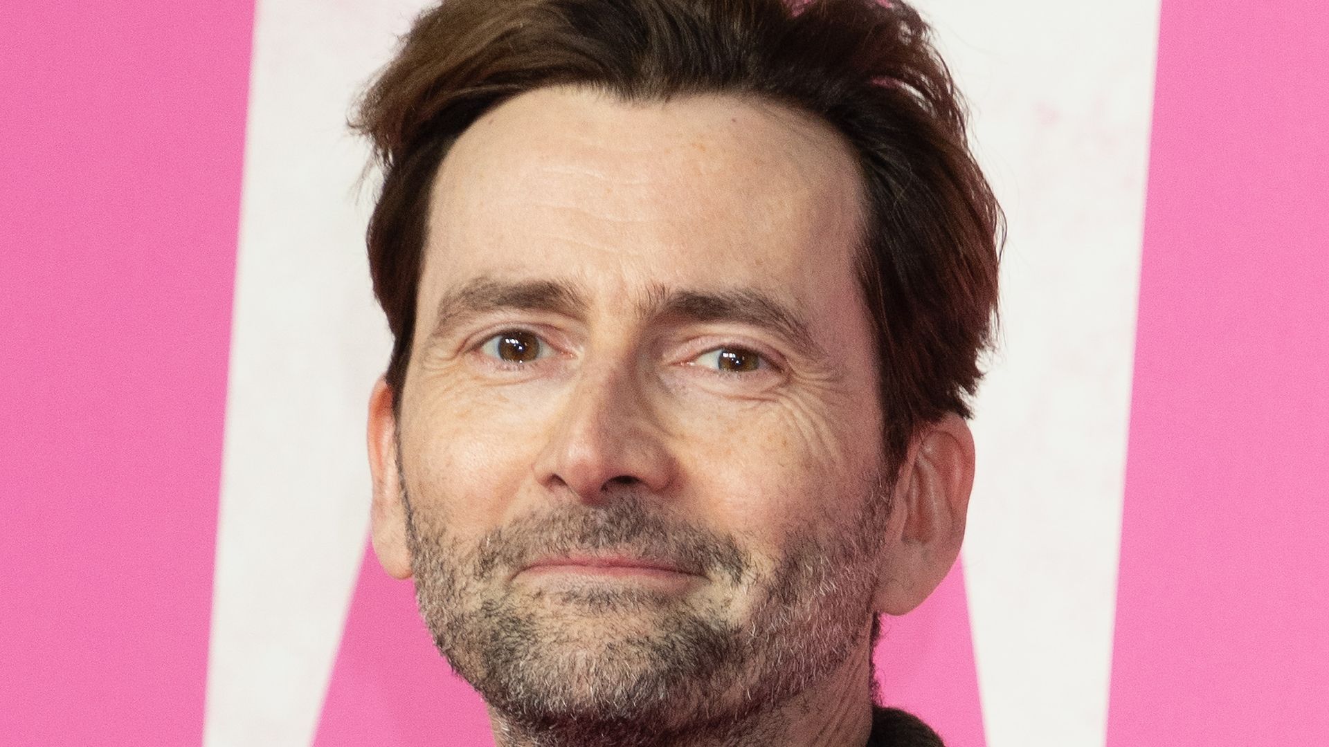 David Tennant in a suit in front of a pink and white background