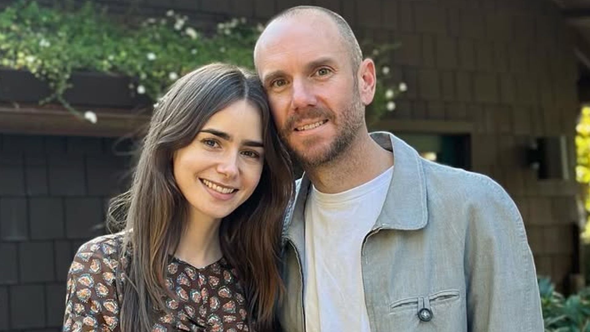 Lily Collins and Charlie McDowell smiling for a photo while standing outside a house