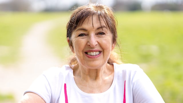 woman smiling in a white top leaning on a gate