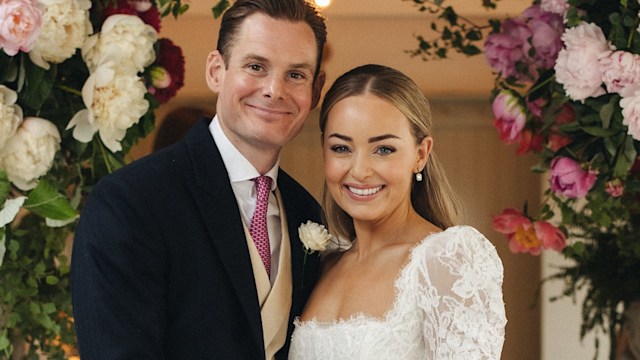 Alice Liveing smiling with her husband Paddy underneath a floral arch