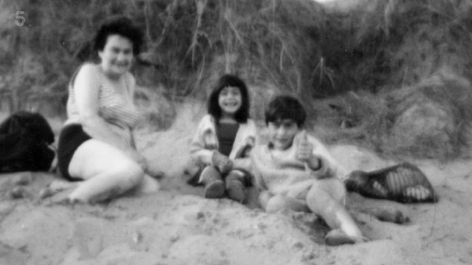 A black-and-white photo of a mother with her son and daughter on the beach