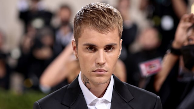 Justin Bieber with his hands crossed standing in a suit while walking red carpet at the MET Gala