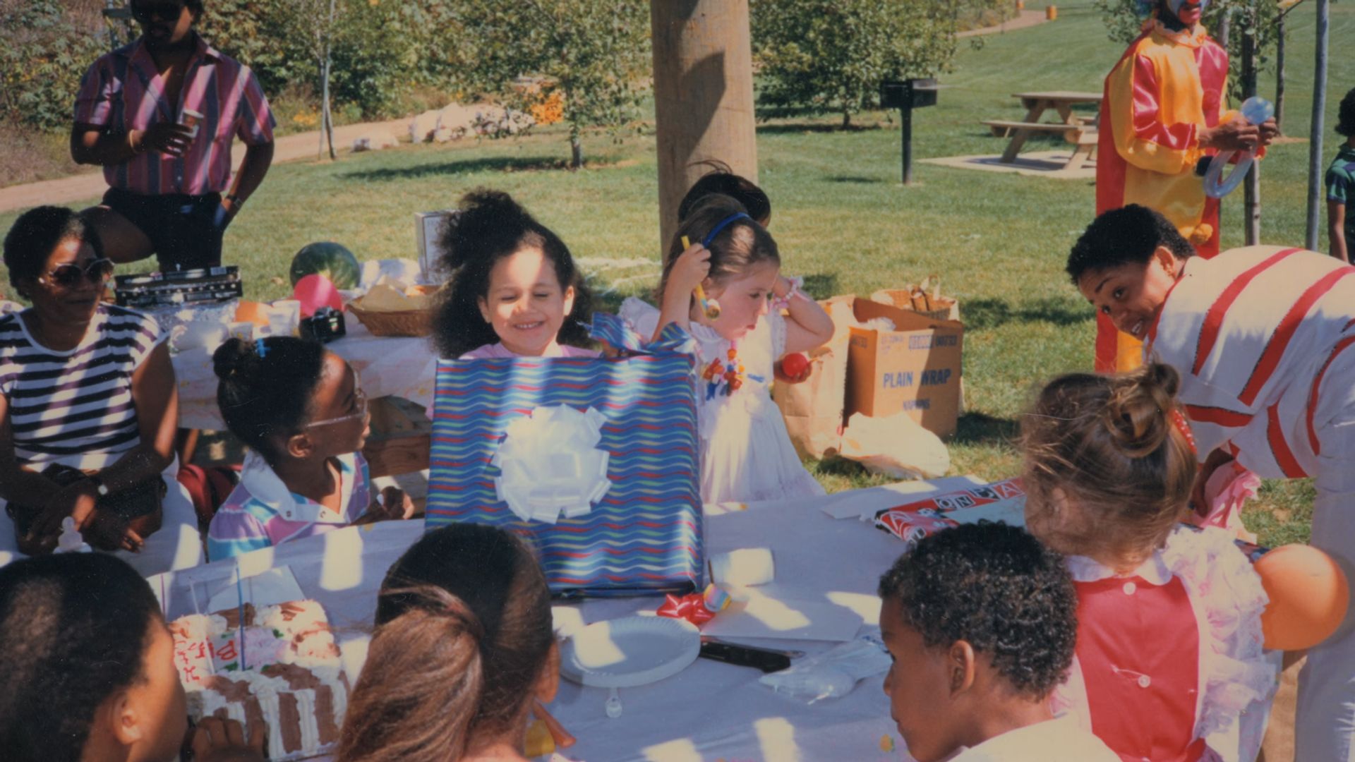 A young Meghan Markle at a birthday party holding a blue present