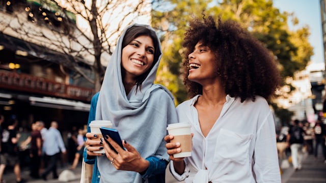 Portrait of two beautiful girls drinking coffee and surfing the net at the street.