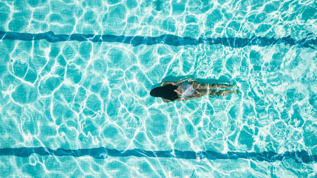 Drone view on teenage girl diving in blue swimming pool