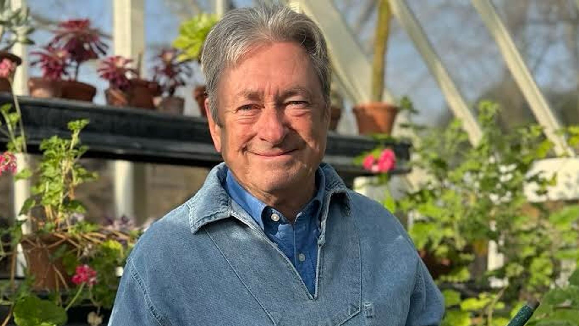 Alan Titchmarsh holding a watering can while standing in his greenhouse