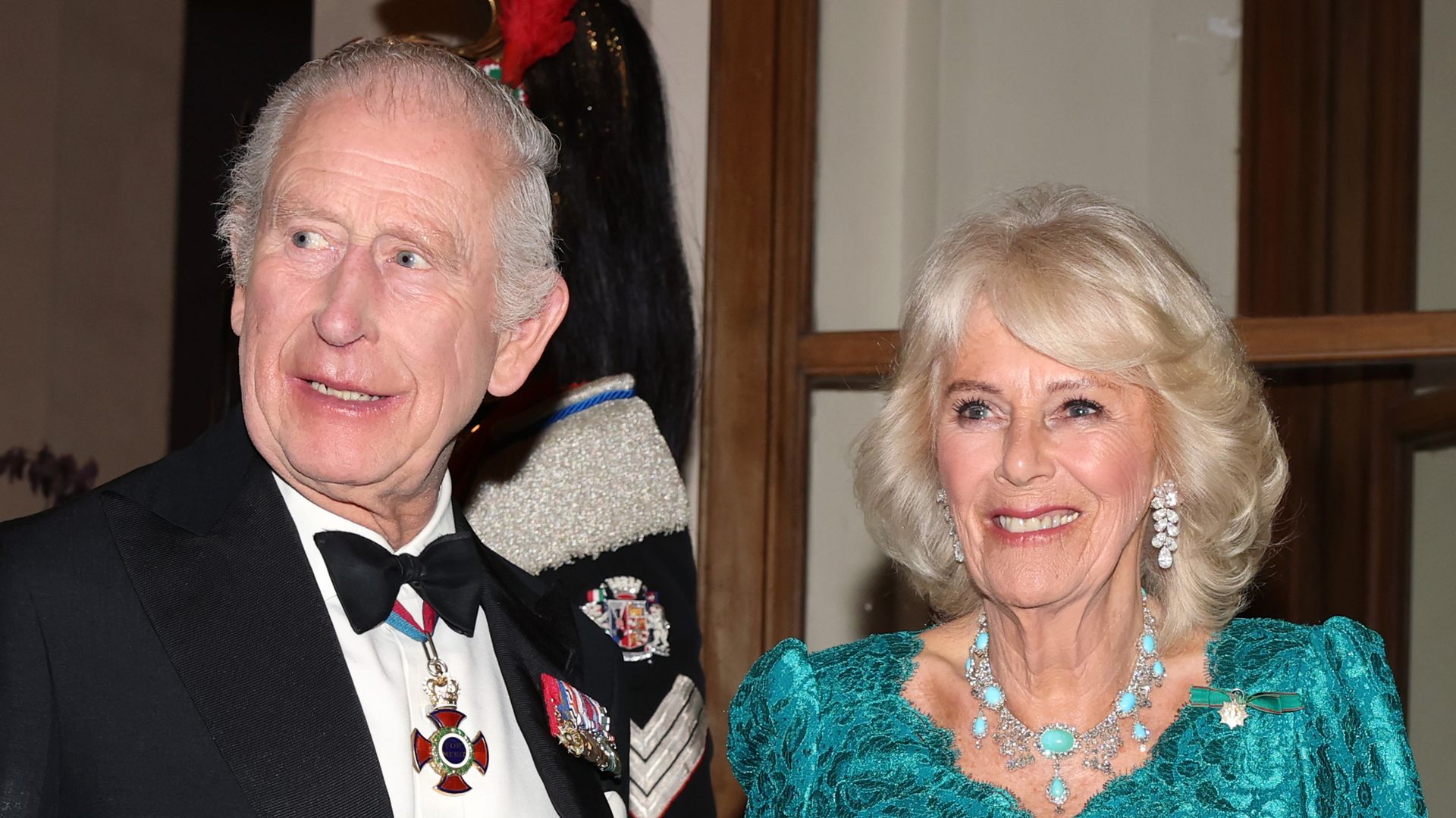 King Charles in a black tuxedo and Queen Camilla in an emerald dress