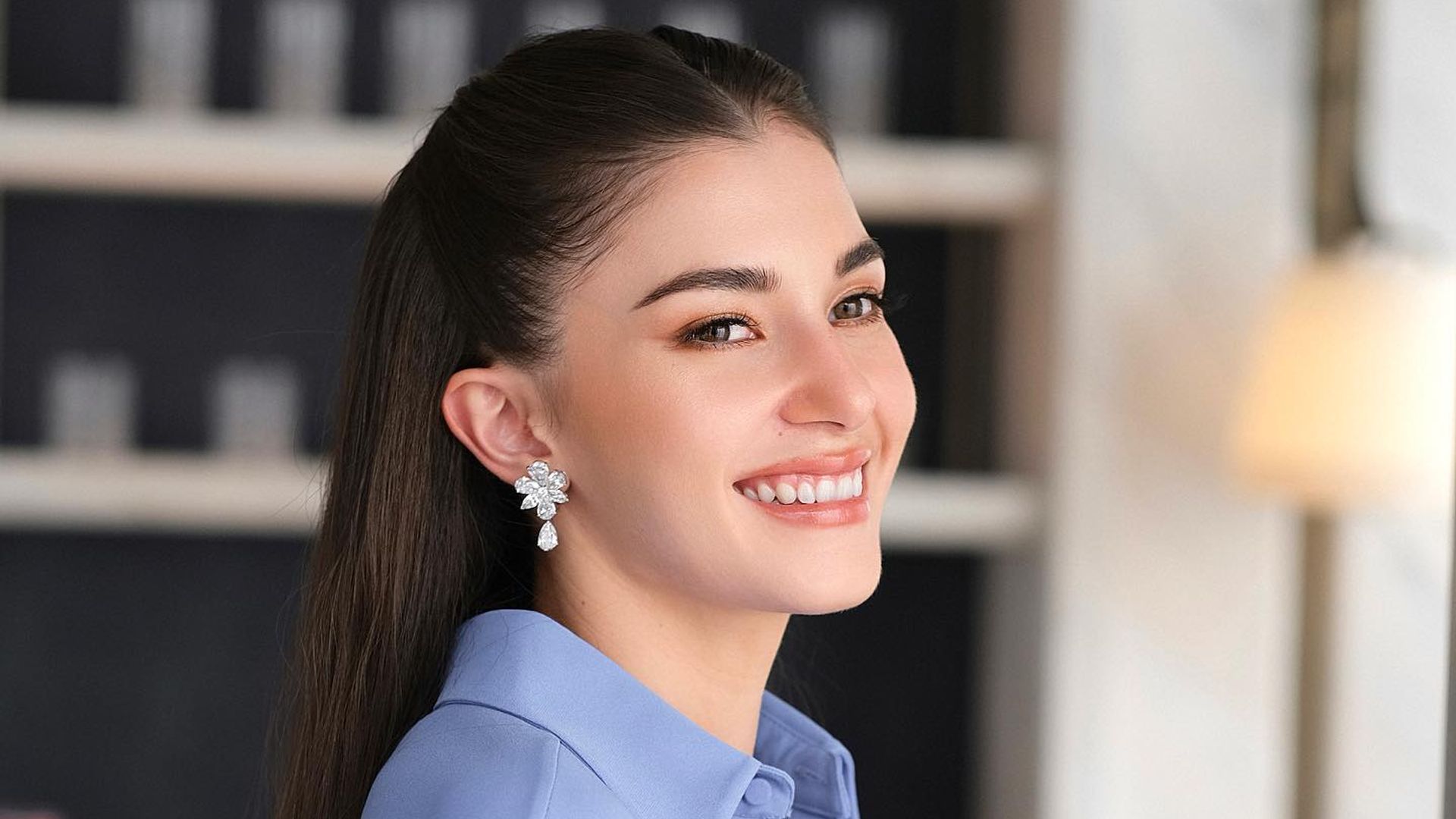 Princess Anisha Rosnah of Brunei smiles for the camera in a blue blouse and diamond earring look