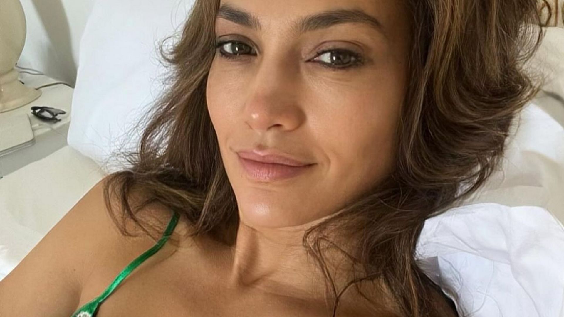 Photo shared by Jennifer Lopez on Instagram August 2023 where she is in bed with no make-up wearing a green lace négligée