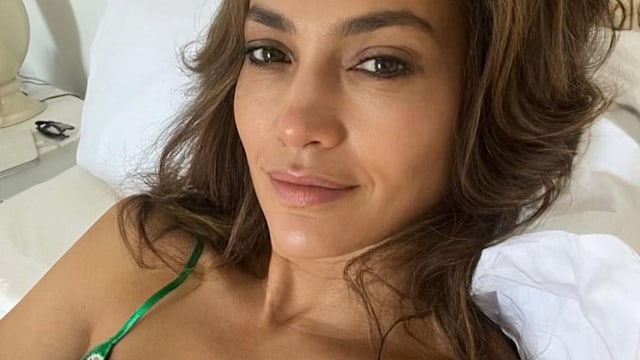 Photo shared by Jennifer Lopez on Instagram August 2023 where she is in bed with no make-up wearing a green lace négligée