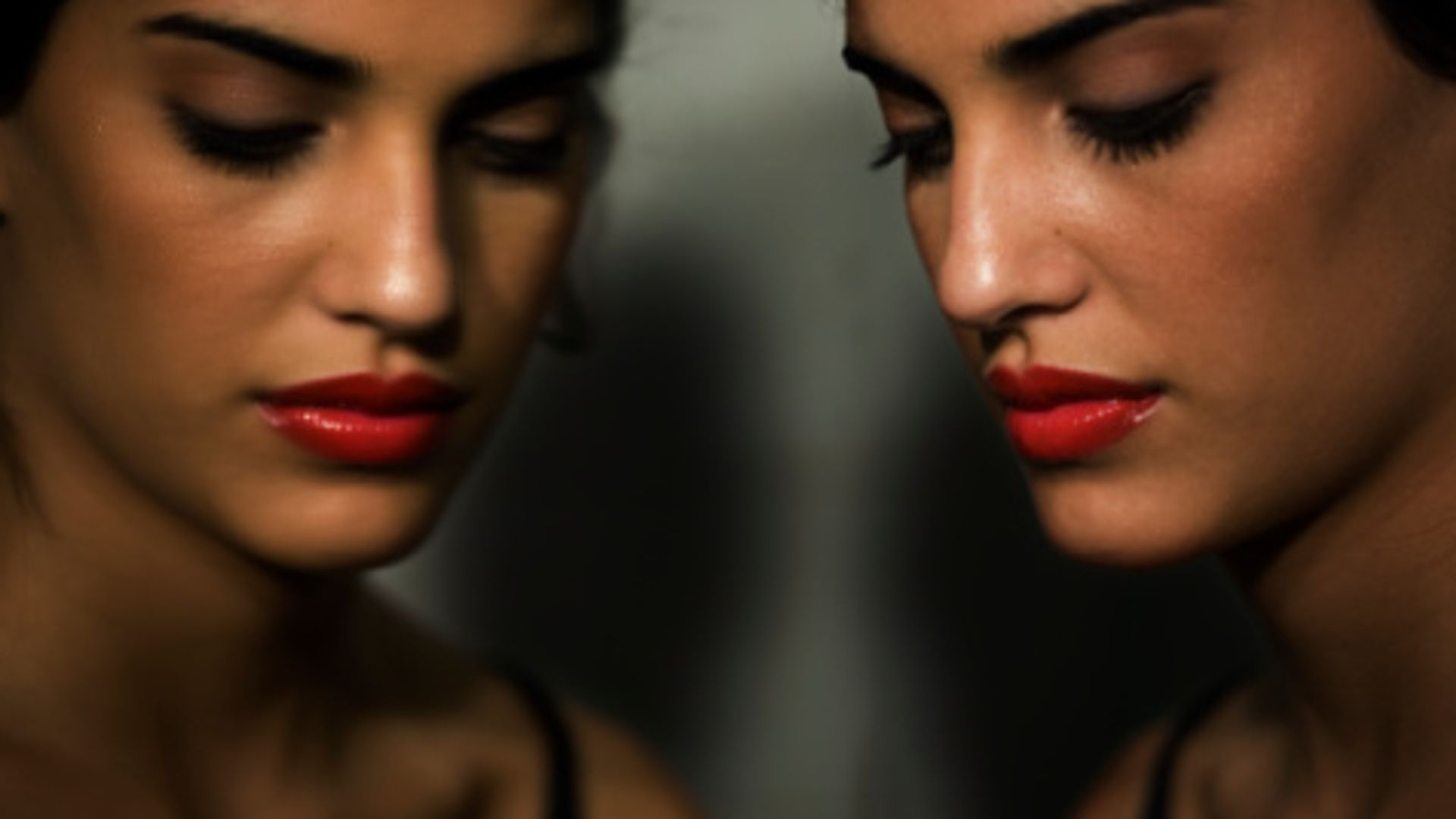 A model with red lipstick whose face is reflected in a mirror 