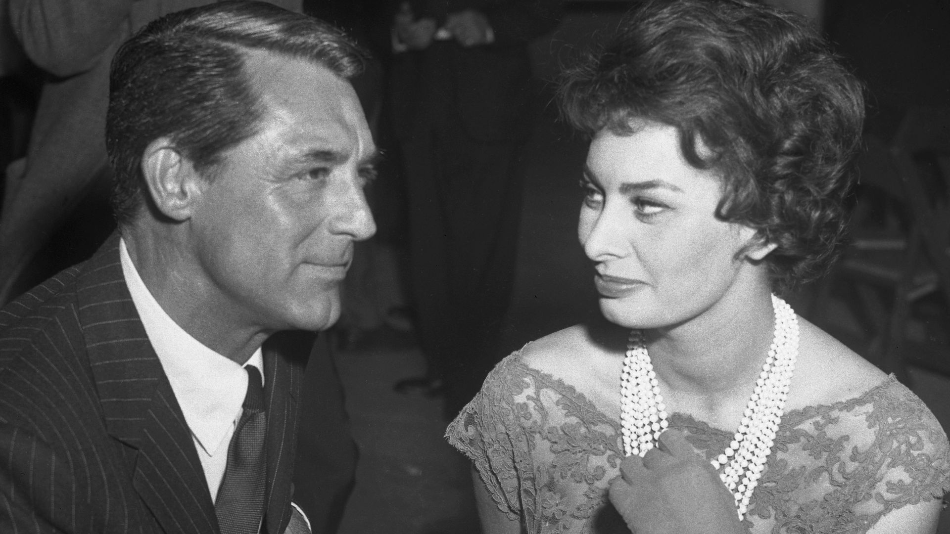 Sophia Loren with a pearl necklace sitting at a table with Cary Grant
