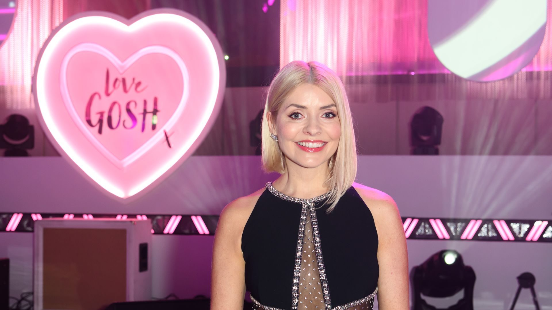 Holly Willoughby smiling in front of a pink heart