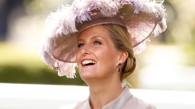 Sophie in blush feathered hat and dress looking up