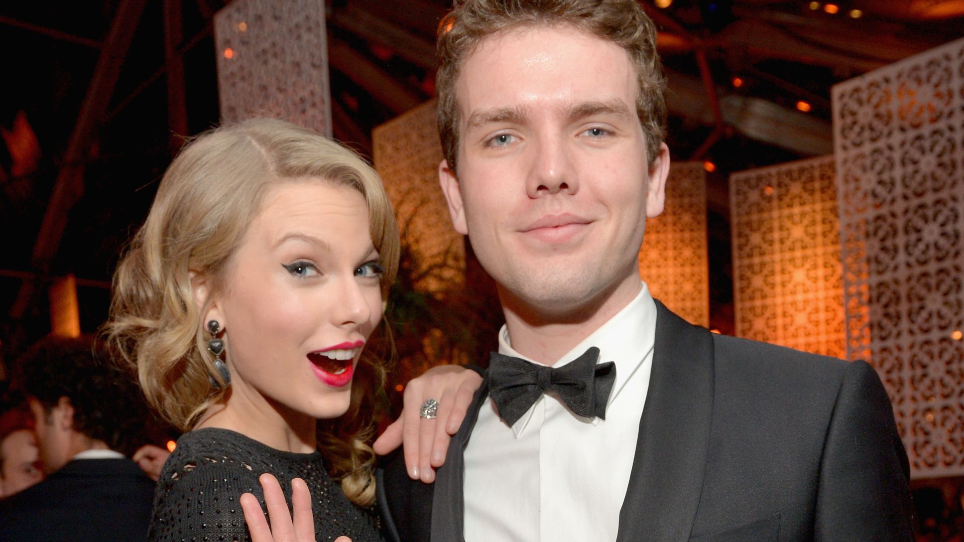 Taylor Swift posing and waving with her brother Austin Swift at a fancy event