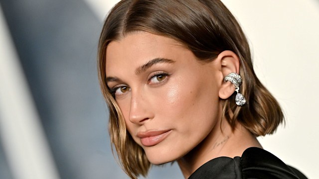 Hailey Bieber looking over her shoulder wearing a black dress at Oscars party