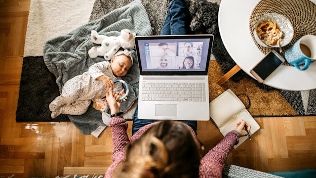 Cute little baby playing on the floor by her working mother.  Young mother with a baby and a dog, sitting on the floor and working. High angle of view.